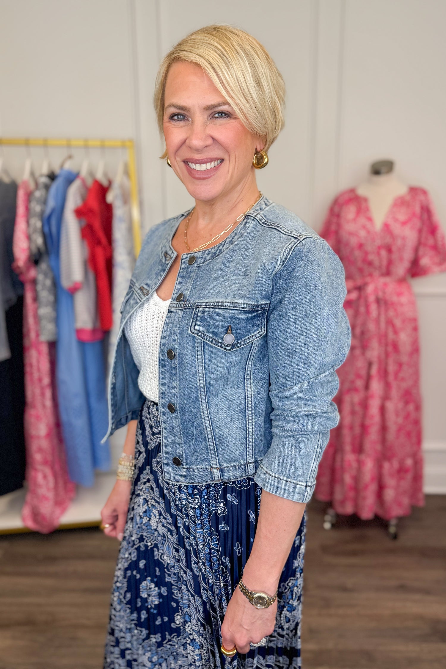 Side view of woman wearing Medium Wash Collarless Denim Jacket by Just Black Denim with top and skirt. 