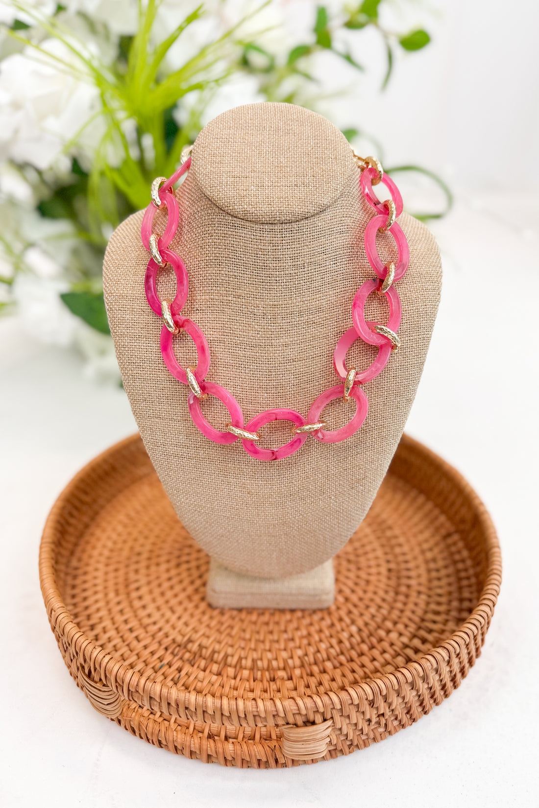 Necklace on a mannequin bust with a woven tray and floral background