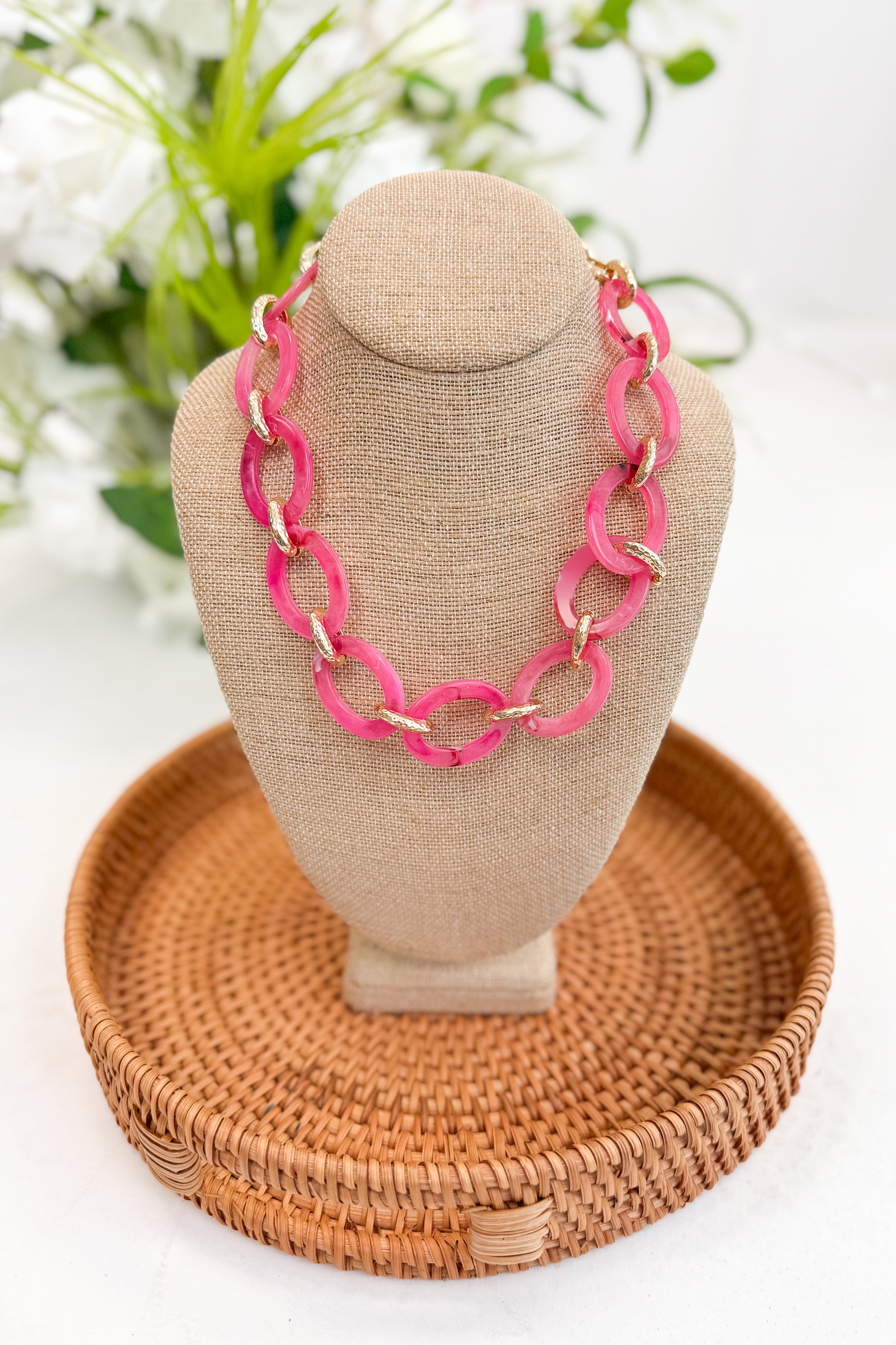 Necklace on a mannequin bust with a woven tray and floral background