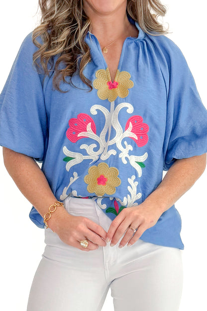 Front detail view of woman wearing Blue Floral Embroidered Top with jeans against white studio background.