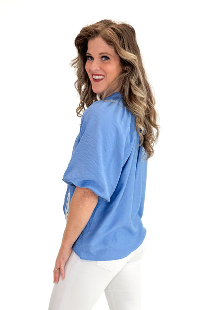 Side view of woman wearing Blue Floral Embroidered Top with jeans against white studio background.