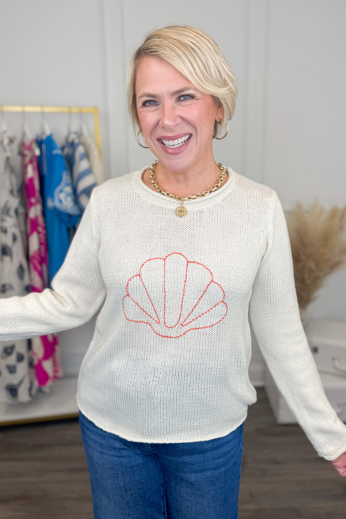 Woman wearing a white sweater with a red shell design in a clothing store.