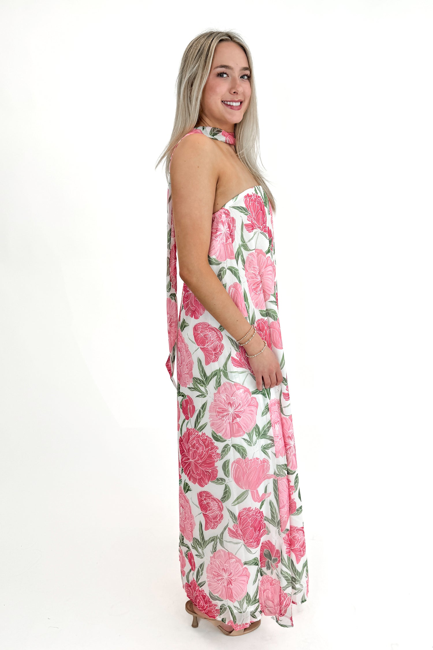 Side view of woman wearing Pink Floral Maxi Dress With Convertible Scarf against white studio background.