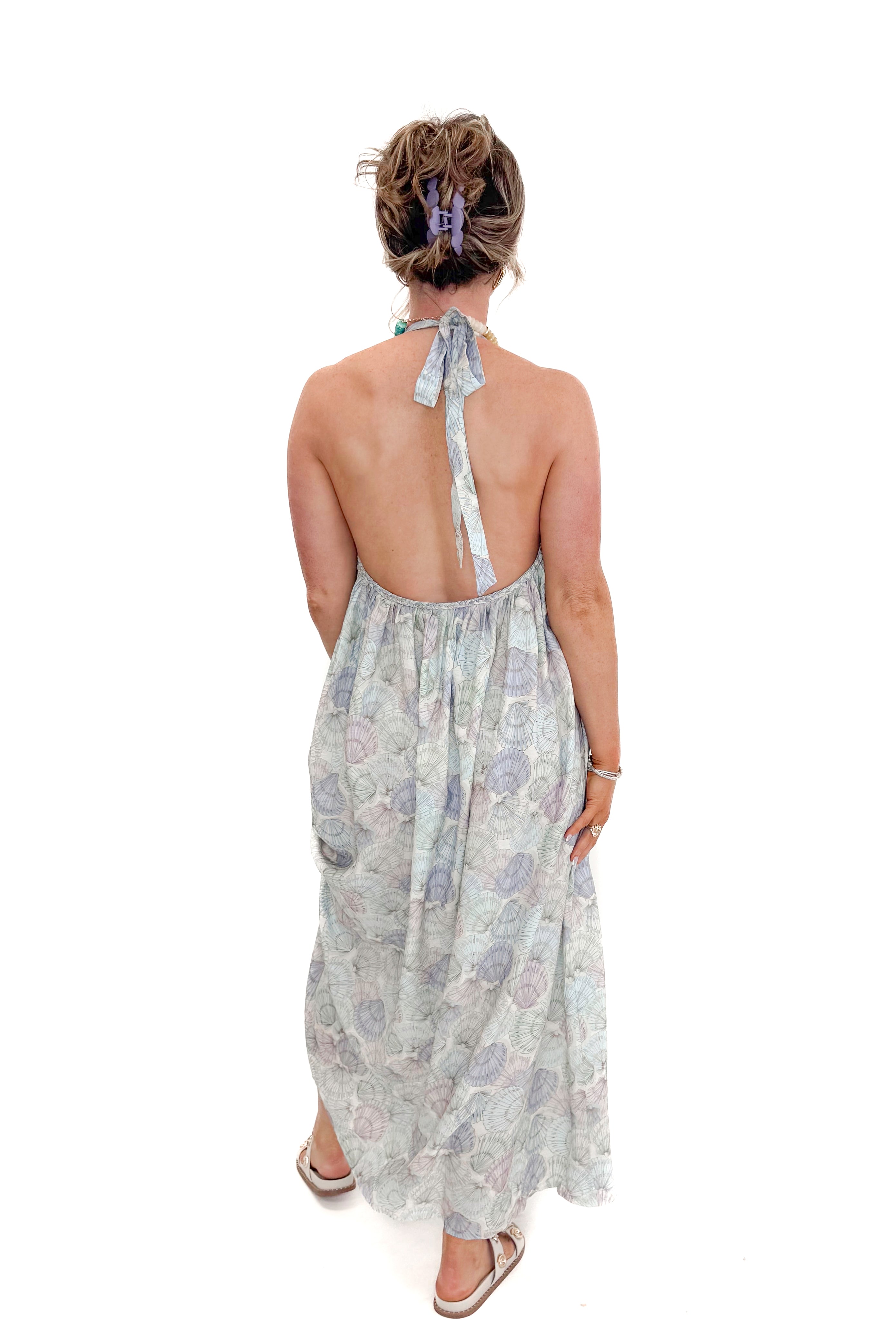 Back view of woman wearing Blue &amp; Multi Shell Print Halter Neck Dress with sandals against white studio background.
