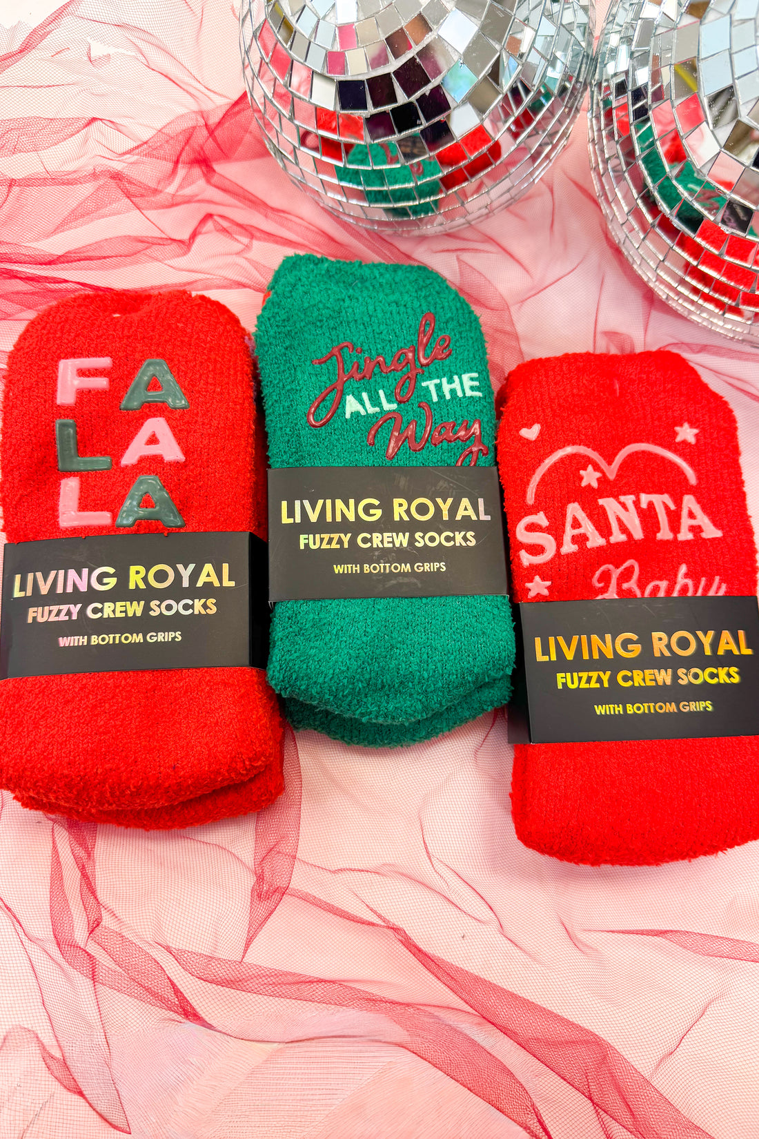 Three pairs of fuzzy crew socks with festive designs on a pink background with disco balls.