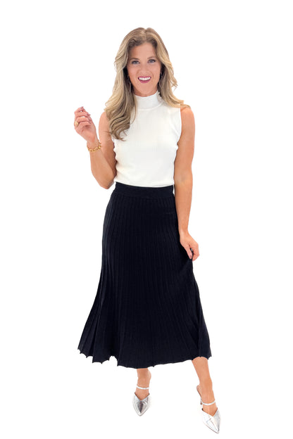 Front view of woman wearing Off White Pearl Detail Mock Neck Top with Black Pleated Sweater Skirt against white studio background.