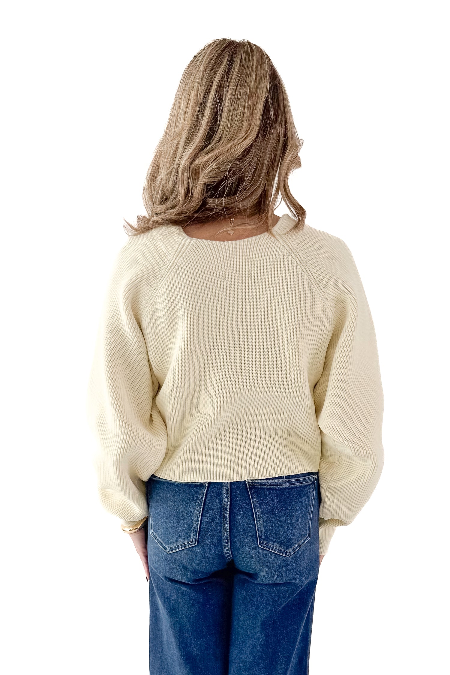 Back view of woman wearing Ivory Ribbed V-neck Cardigan with jeans against white studio background.