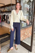Front view of woman wearing Ivory Ribbed V-neck Cardigan with jeans against boutique door open background.
