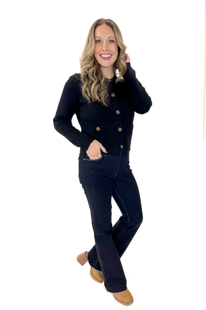 Side view of woman wearing Black Button Detail Cardigan with jeans against white studio background.