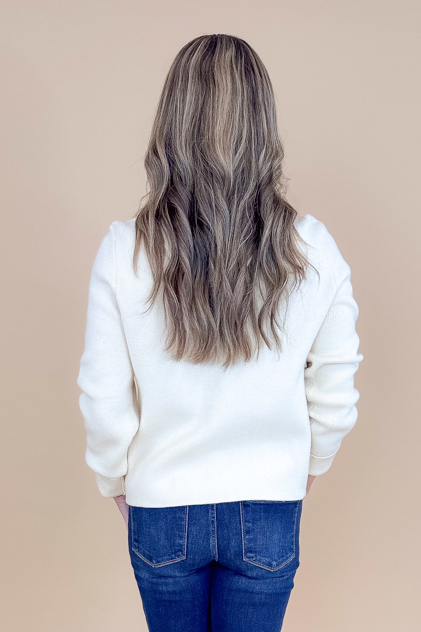 Back view of woman wearing Oatmeal Button Detail Cardigan with jeans against tan studio background.
