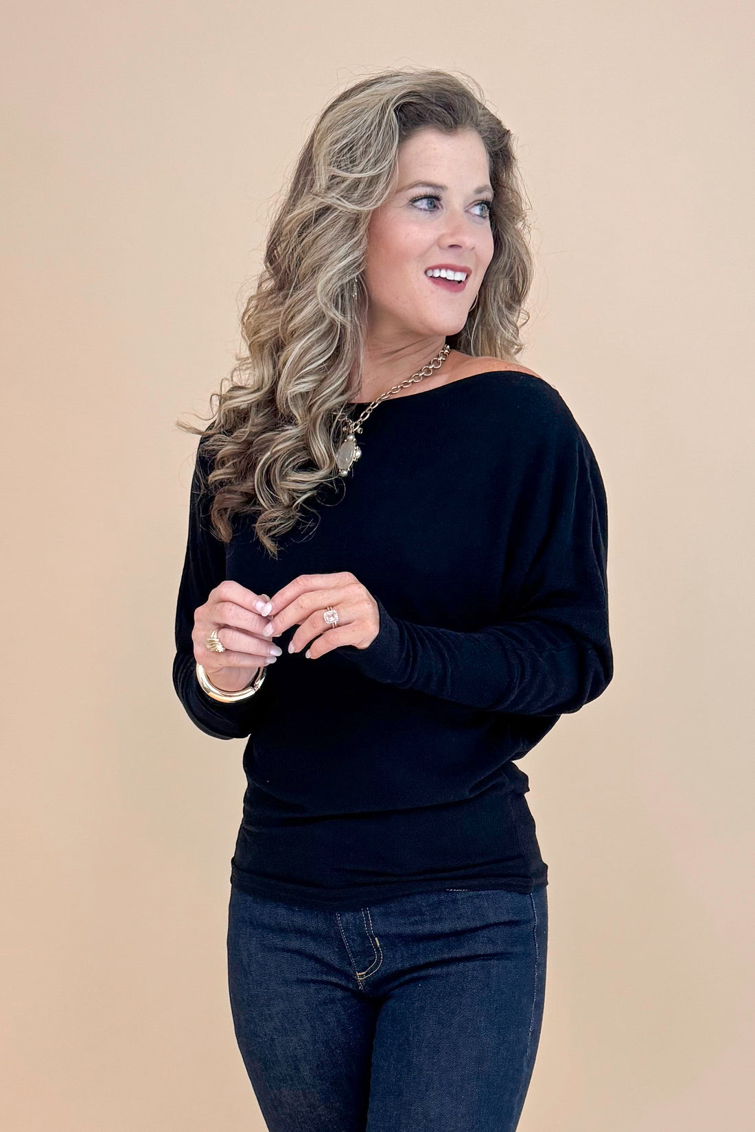 Front view picture of woman wearing Black Wide Neck Long Sleeve Top and jeans against a tan background.