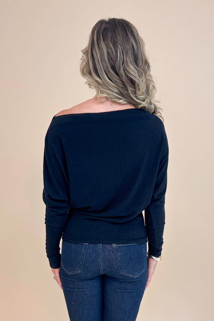 Back view picture of woman wearing Black Wide Neck Long Sleeve Top and jeans against a tan background.