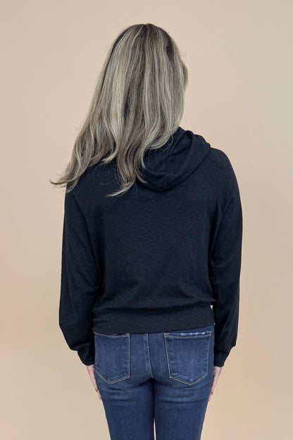 Back view of woman wearing Black Hooded Sweatshirt and jeans with a tan background. 