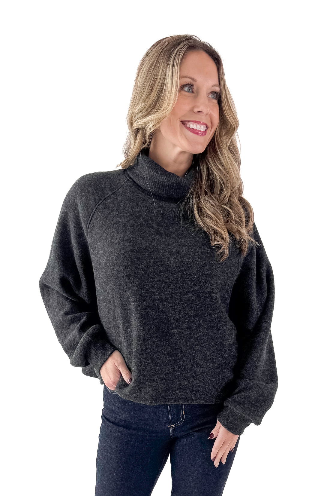 Front view of woman wearing charcoal sweater with jeans against white studio background.