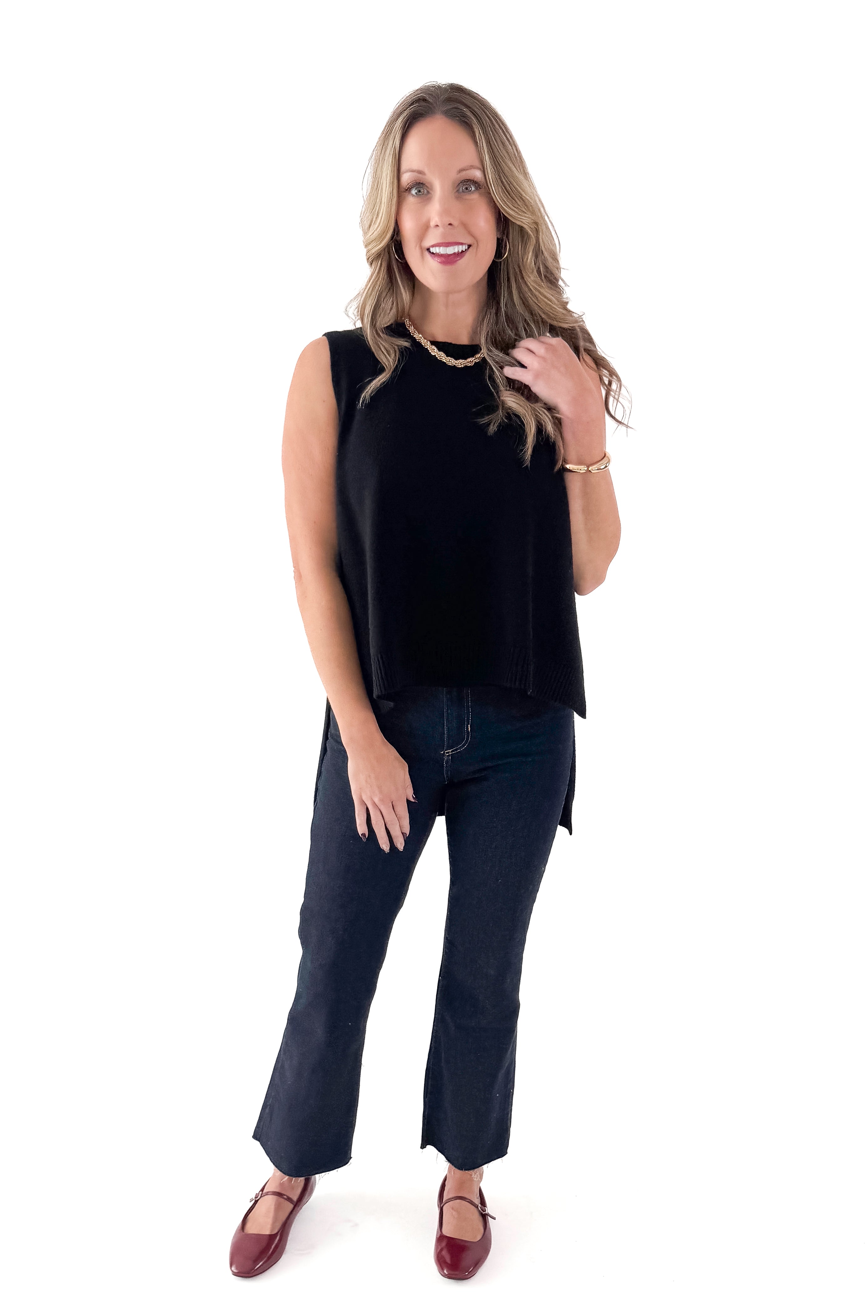 Front view of woman wearing black sweater with jeans against white studio background.