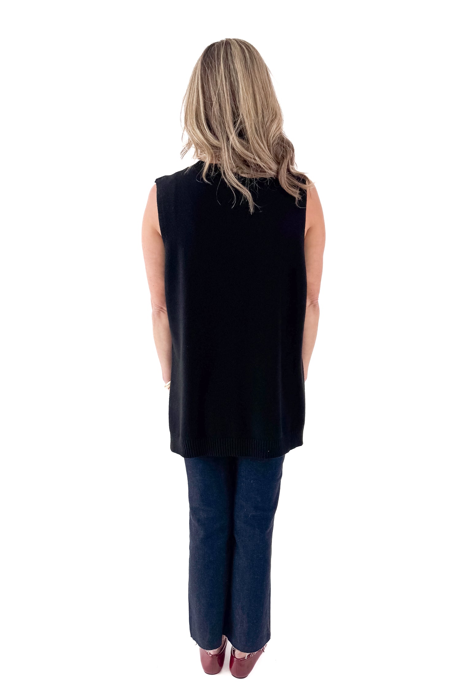 Back view of woman wearing black sweater with jeans against white studio background.