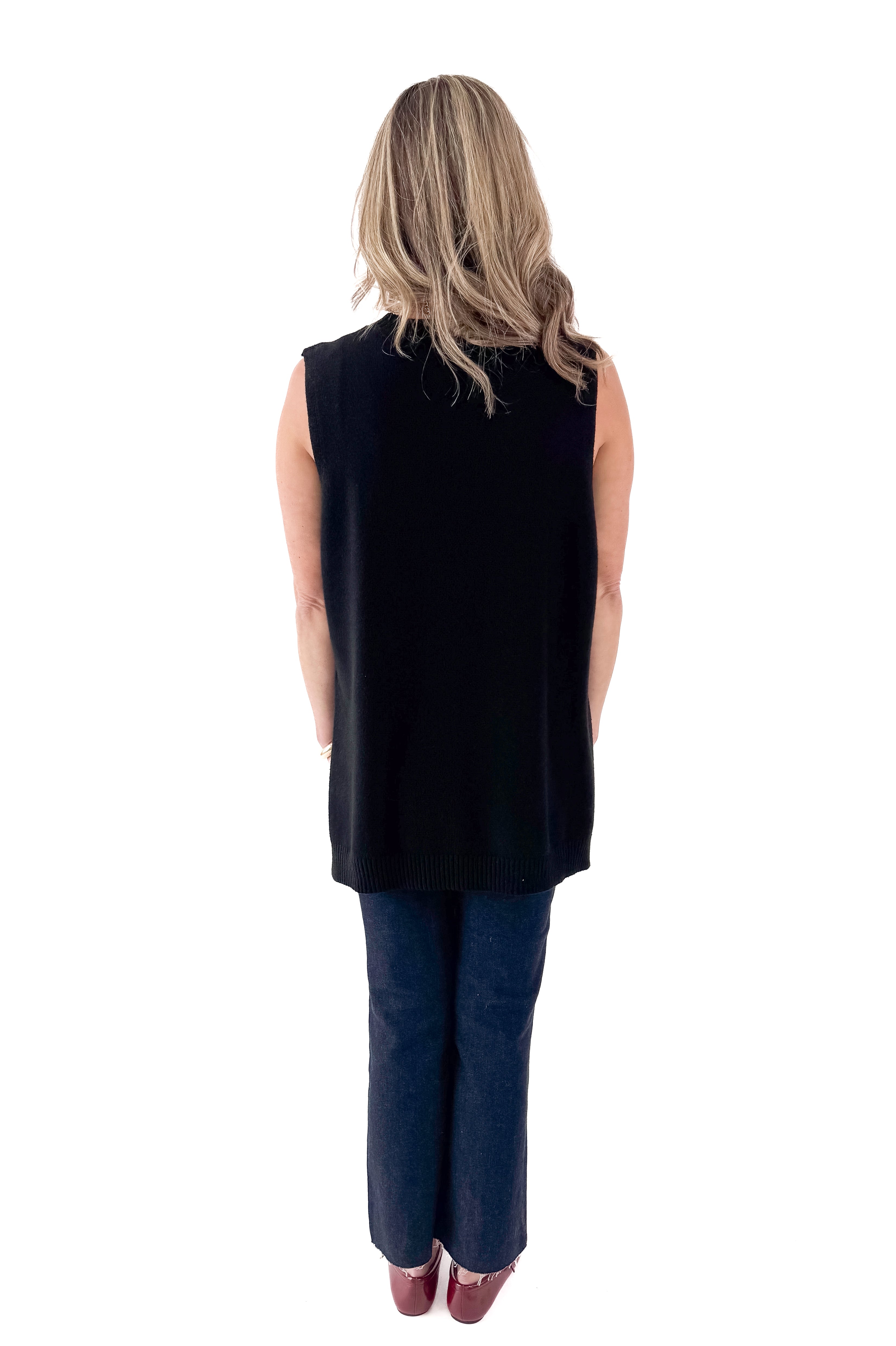 Back view of woman wearing black sweater with jeans against white studio background.