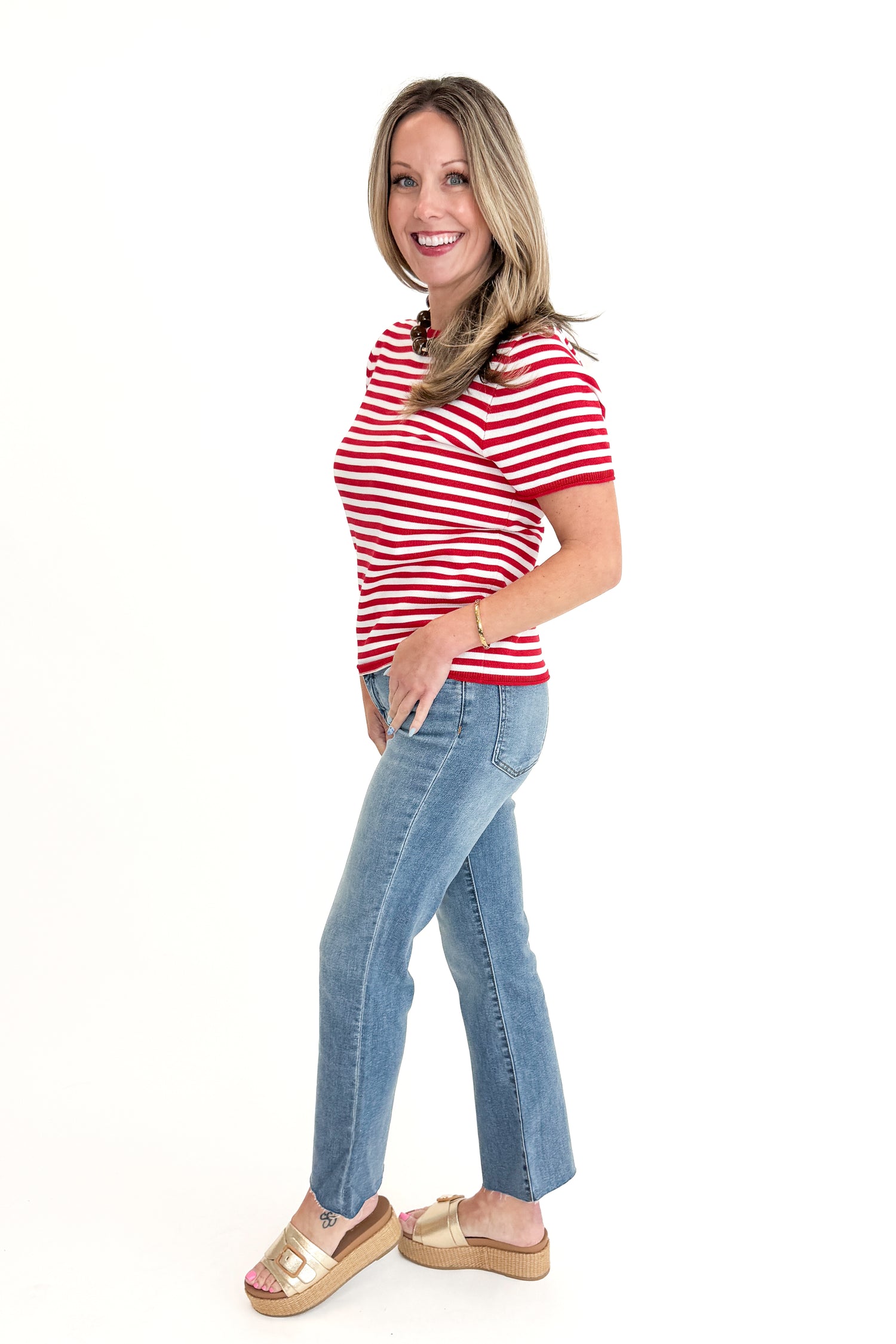 Side view of woman wearing Red &amp; White Striped Short Sleeve Sweater with jeans against white studio background.