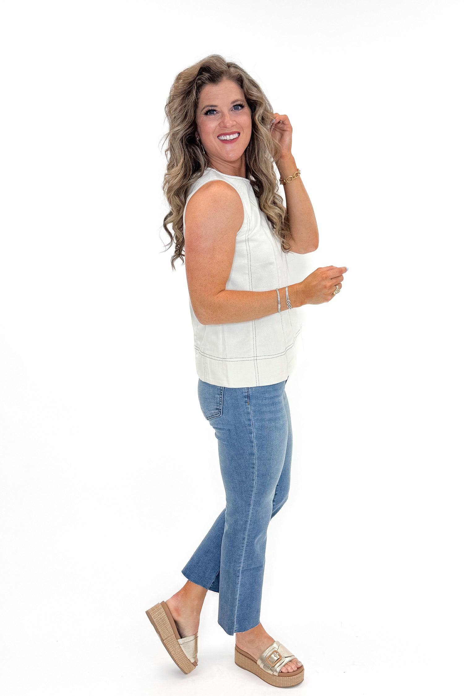 Side view of woman wearing Cream With Black Stitch Detail Tank with jeans against white studio background.