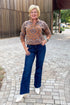 Front view of woman wearing Swagger Boutique’s Camel Bandana Print Half Zip Sweater with jeans standing outside on a brick path.