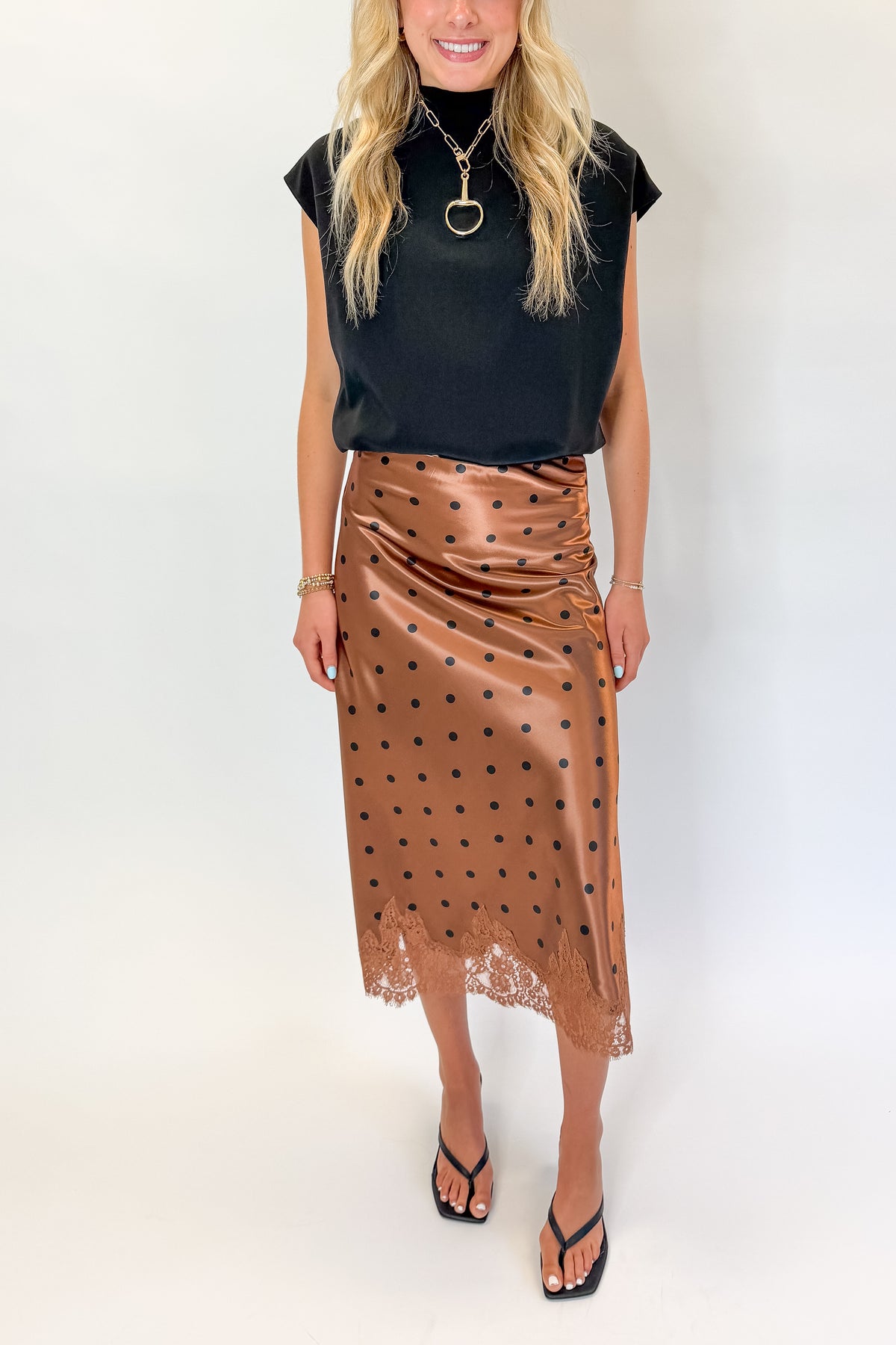 Front detail view of woman wearing Swagger Boutique’s Camel Polka Dot Satin Skirt with black top against white studio background.
