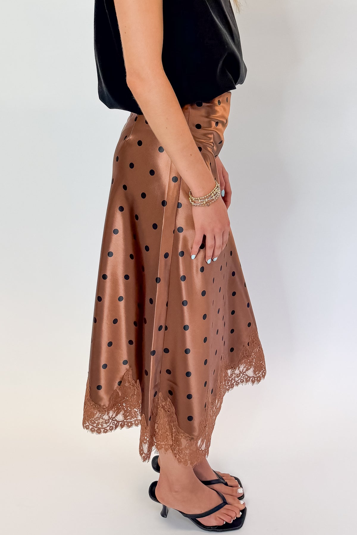 Side detail view of woman wearing Swagger Boutique’s Camel Polka Dot Satin Skirt with black top against white studio background.