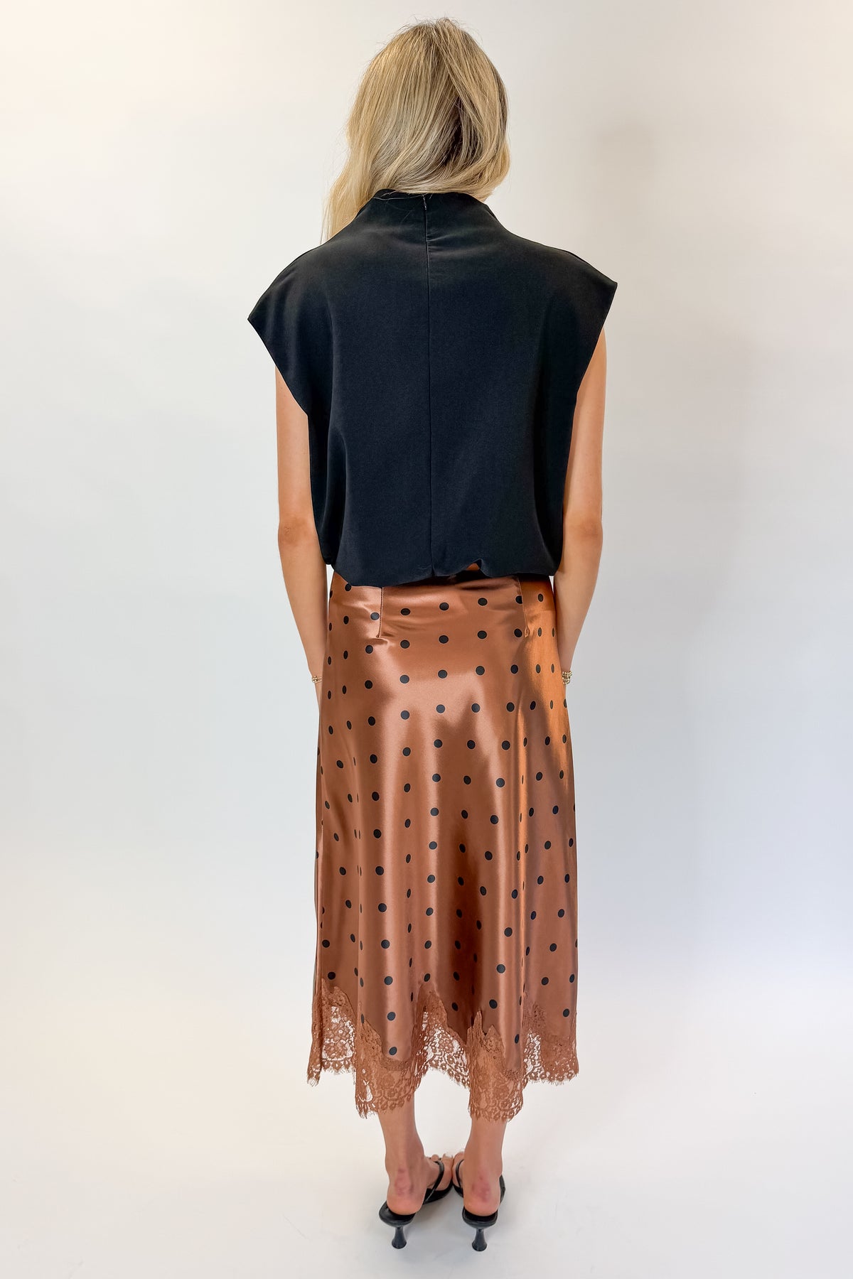 Back view of woman wearing Swagger Boutique’s Camel Polka Dot Satin Skirt with black top against white studio background.
