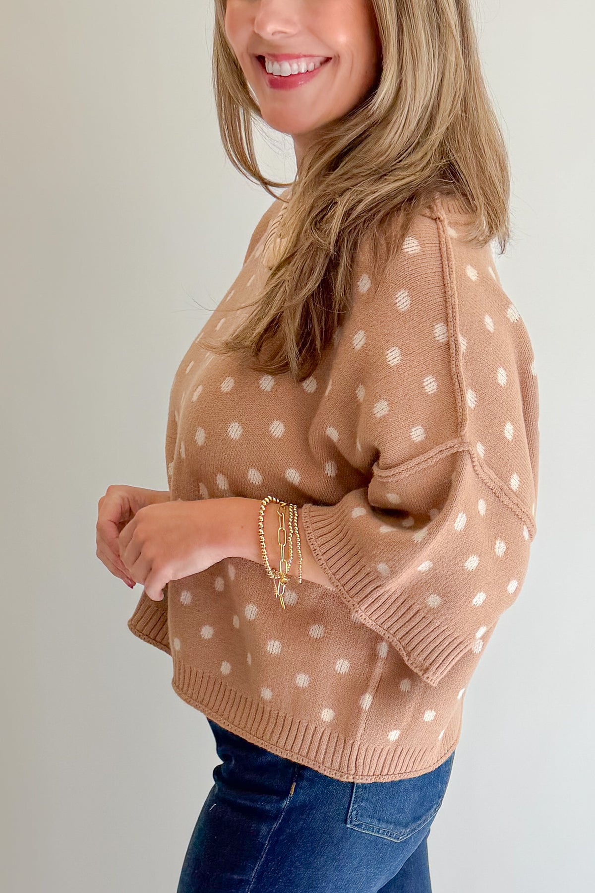 Side detail view of woman wearing Swagger Boutique’s Camel Polka Dot Short Sleeve Sweater by Entro with jeans against white studio background.