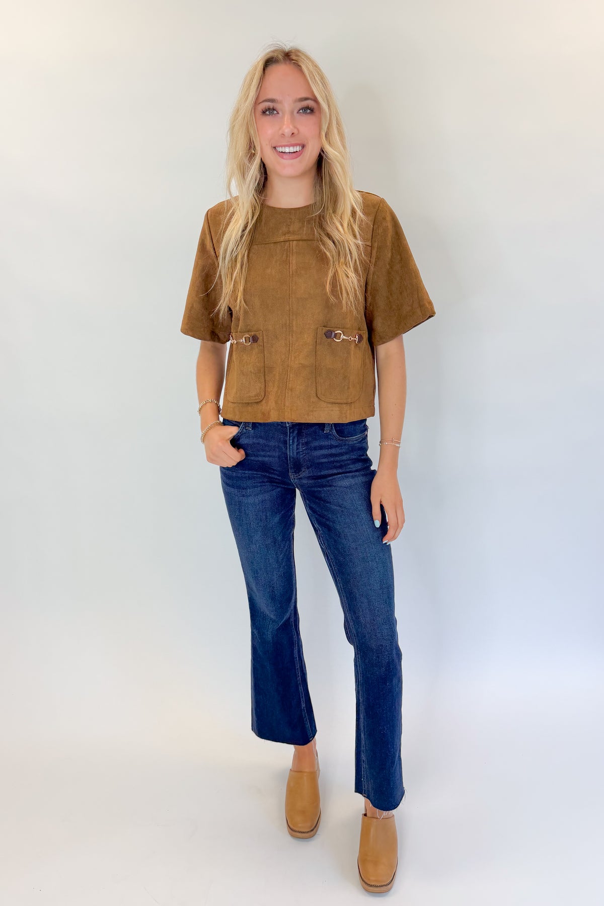 Front view of woman wearing Swagger Boutique’s Camel Suede Horsebit Pocket Top by Entro with jeans against white studio background.