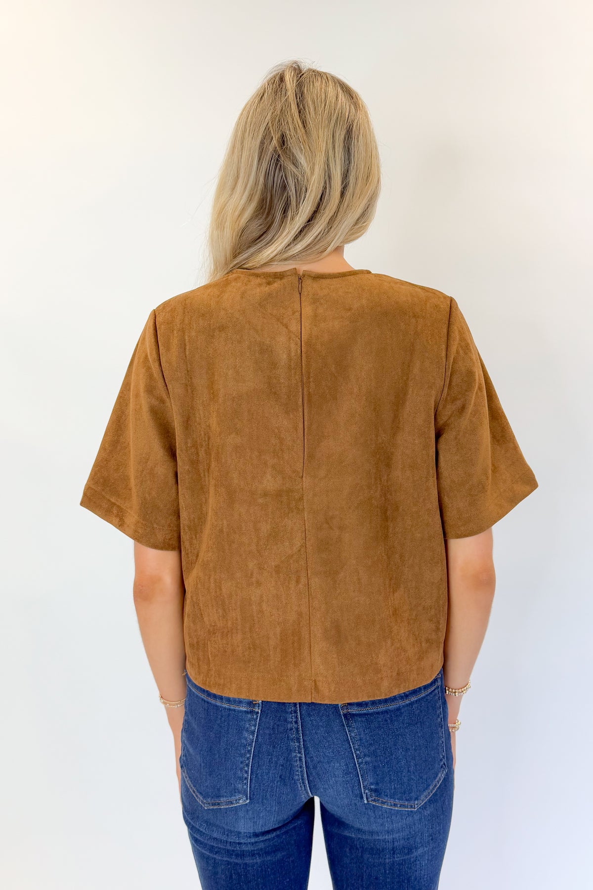 Back view of woman wearing Swagger Boutique’s Camel Suede Horsebit Pocket Top by Entro with jeans against white studio background.