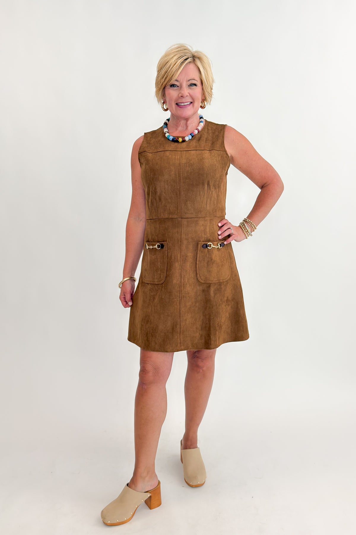 Front view of woman wearing Swagger Boutique’s Camel Suede Mini Dress With Pockets by Entro with clogs against white studio background.