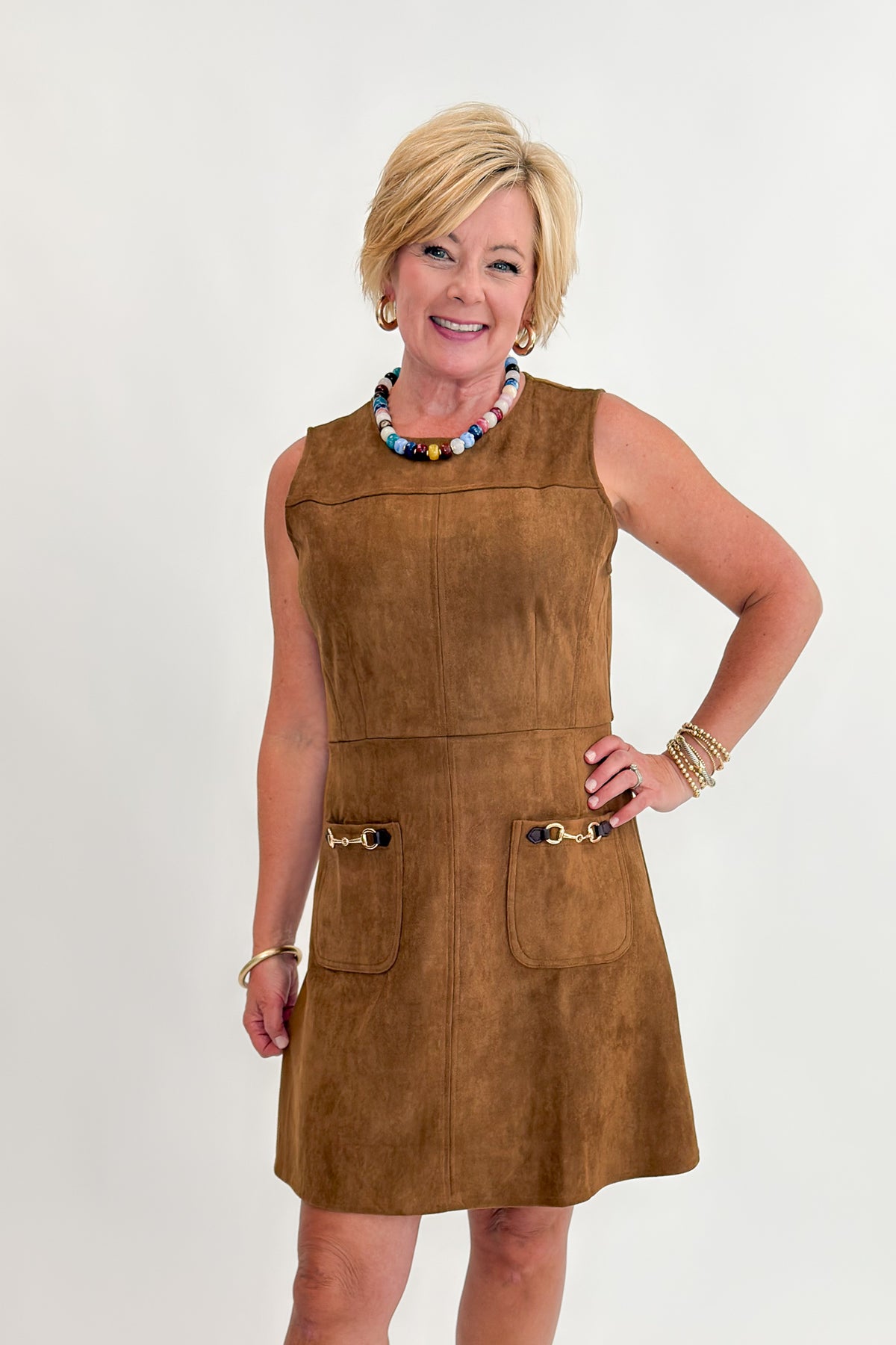 Front view of woman wearing Swagger Boutique’s Camel Suede Mini Dress With Pockets by Entro with clogs against white studio background.