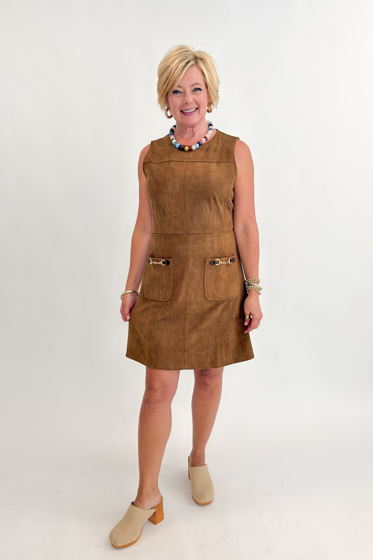 Front view of woman wearing Swagger Boutique’s Camel Suede Mini Dress With Pockets by Entro with clogs against white studio background.