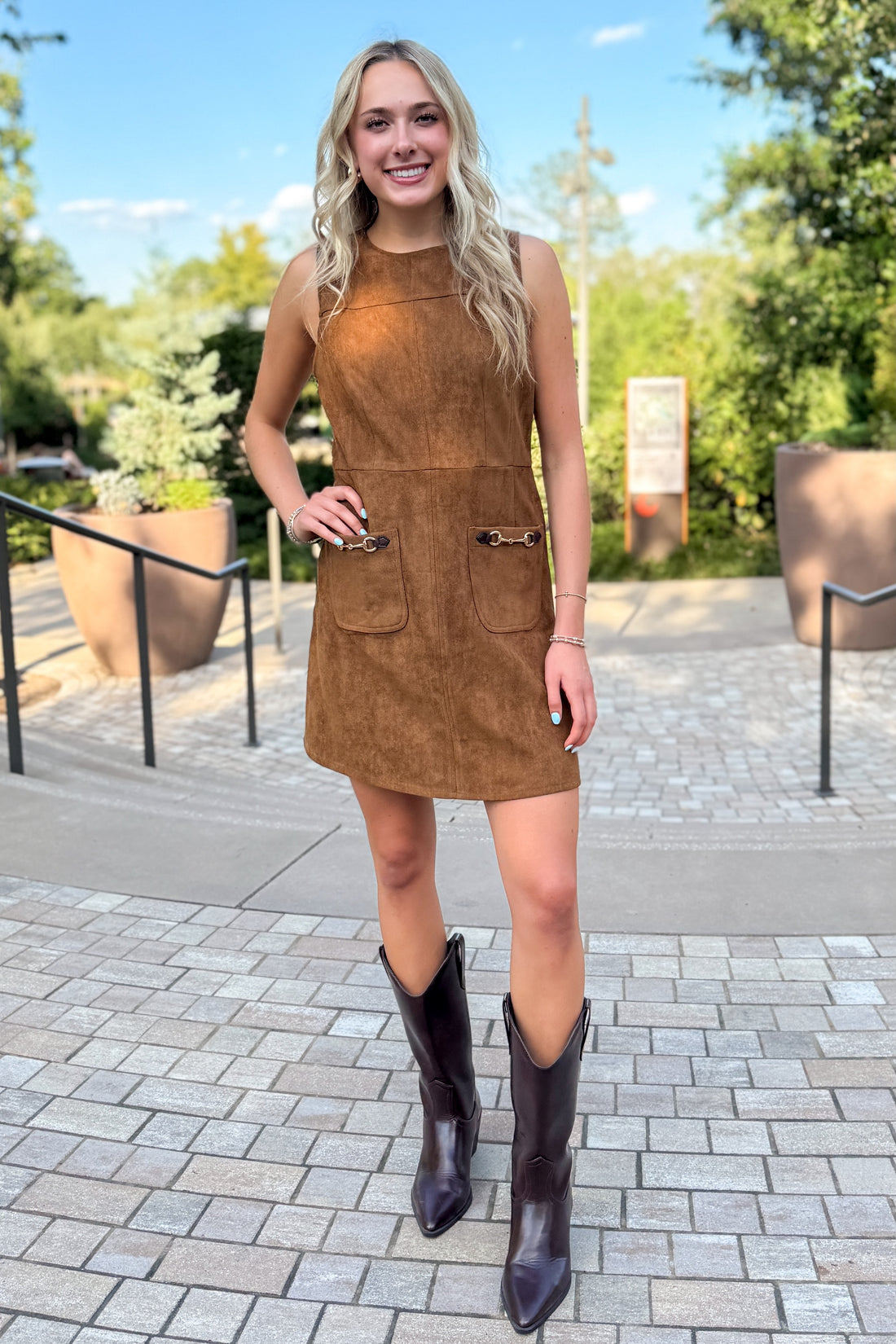 Front view of woman wearing Swagger Boutique’s Camel Suede Mini Dress With Pockets by Entro standing outside by a garden.