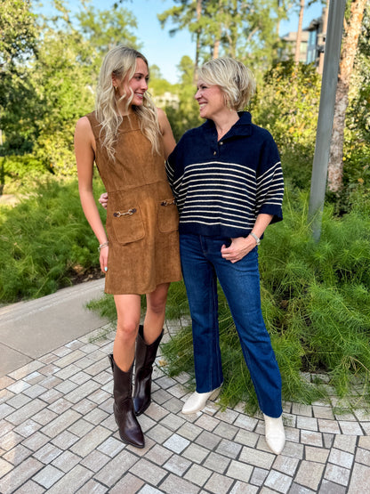 Front view of women wearing Swagger Boutique’s Camel Suede Mini Dress With Pockets by Entro and navy striped sweater standing outside by a garden.