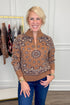 Front view of woman wearing Swagger Boutique’s Camel Bandana Print Half Zip Sweater with jeans with clothing hanging in the background.
