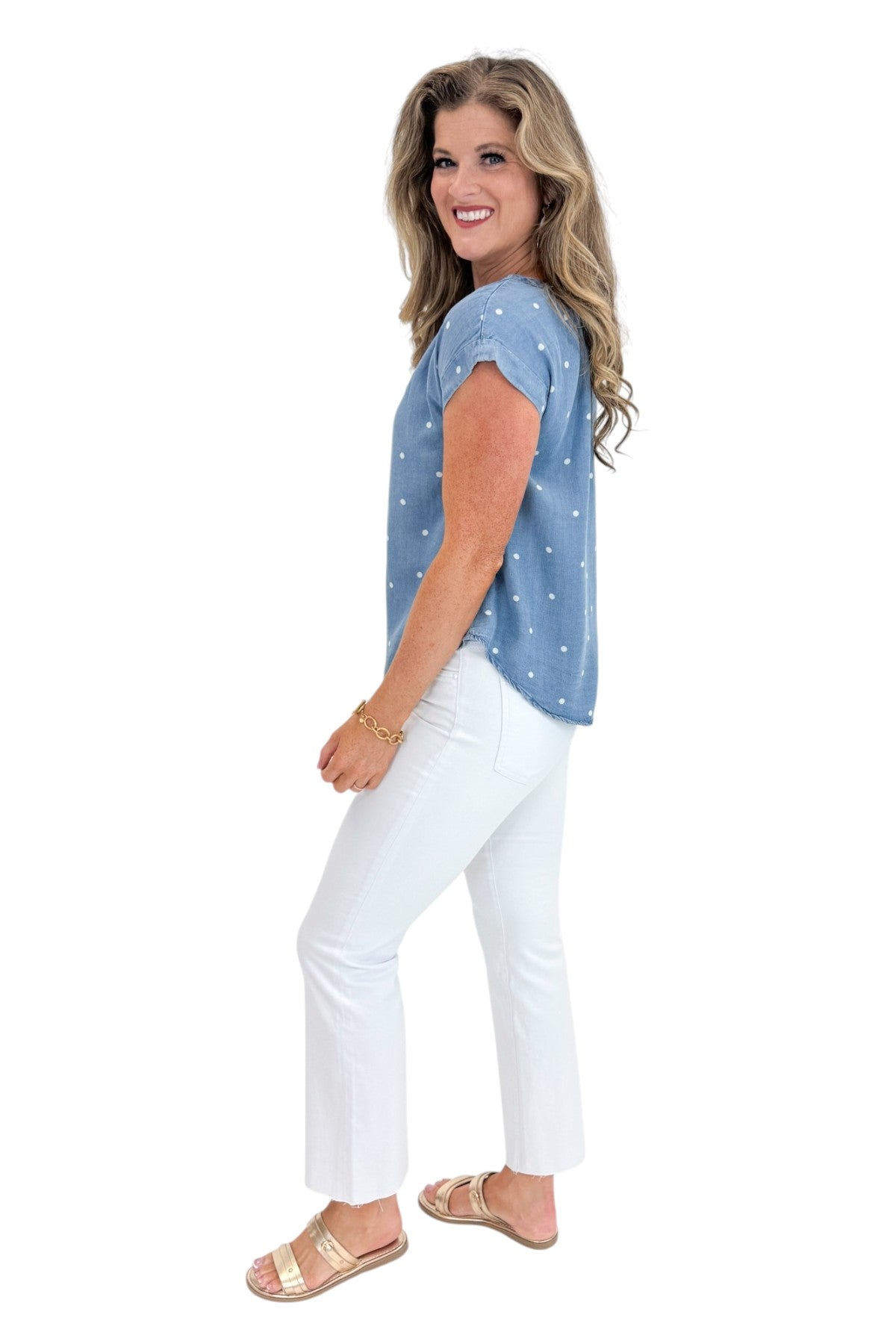 Side view of woman wearing Swagger Boutique’s Chambray Polka Dot Short Sleeve Top with jeans against white studio background.