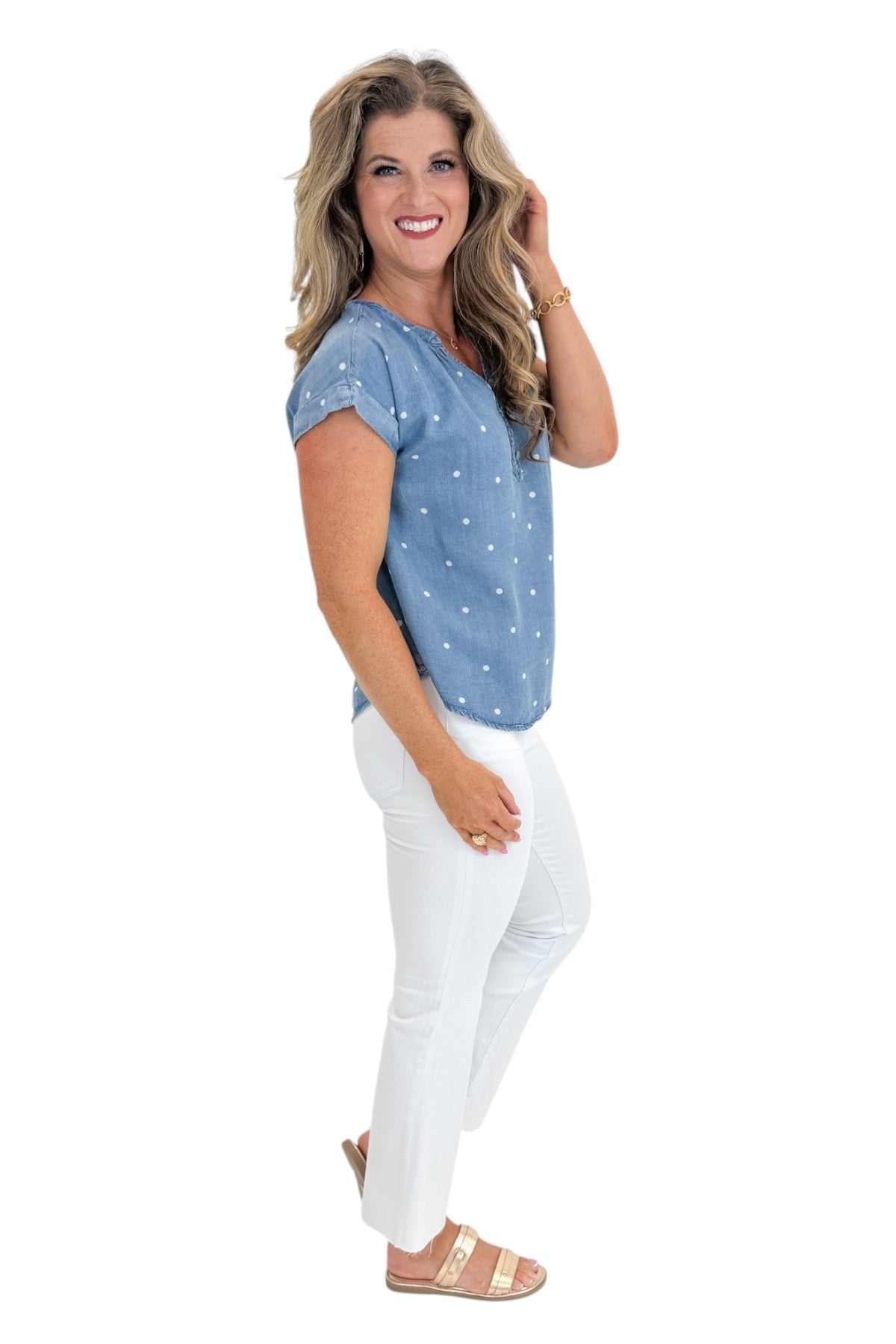 Side view of woman wearing Swagger Boutique’s Chambray Polka Dot Short Sleeve Top with jeans against white studio background.
