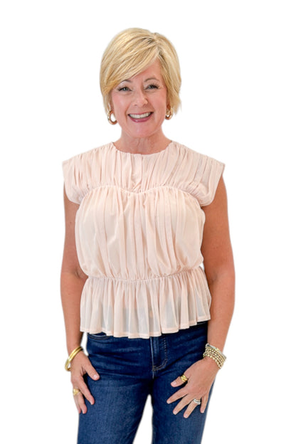 Front view of woman wearing Swagger Boutique’s Champagne Shirred Peplum Top with jeans against white studio background.