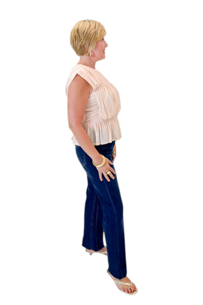 Side view of woman wearing Swagger Boutique’s Champagne Shirred Peplum Top with jeans against white studio background.