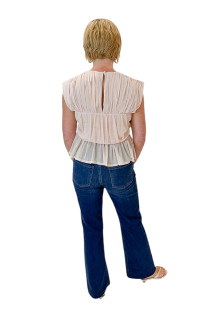 Back view of woman wearing Swagger Boutique’s Champagne Shirred Peplum Top with jeans against white studio background.