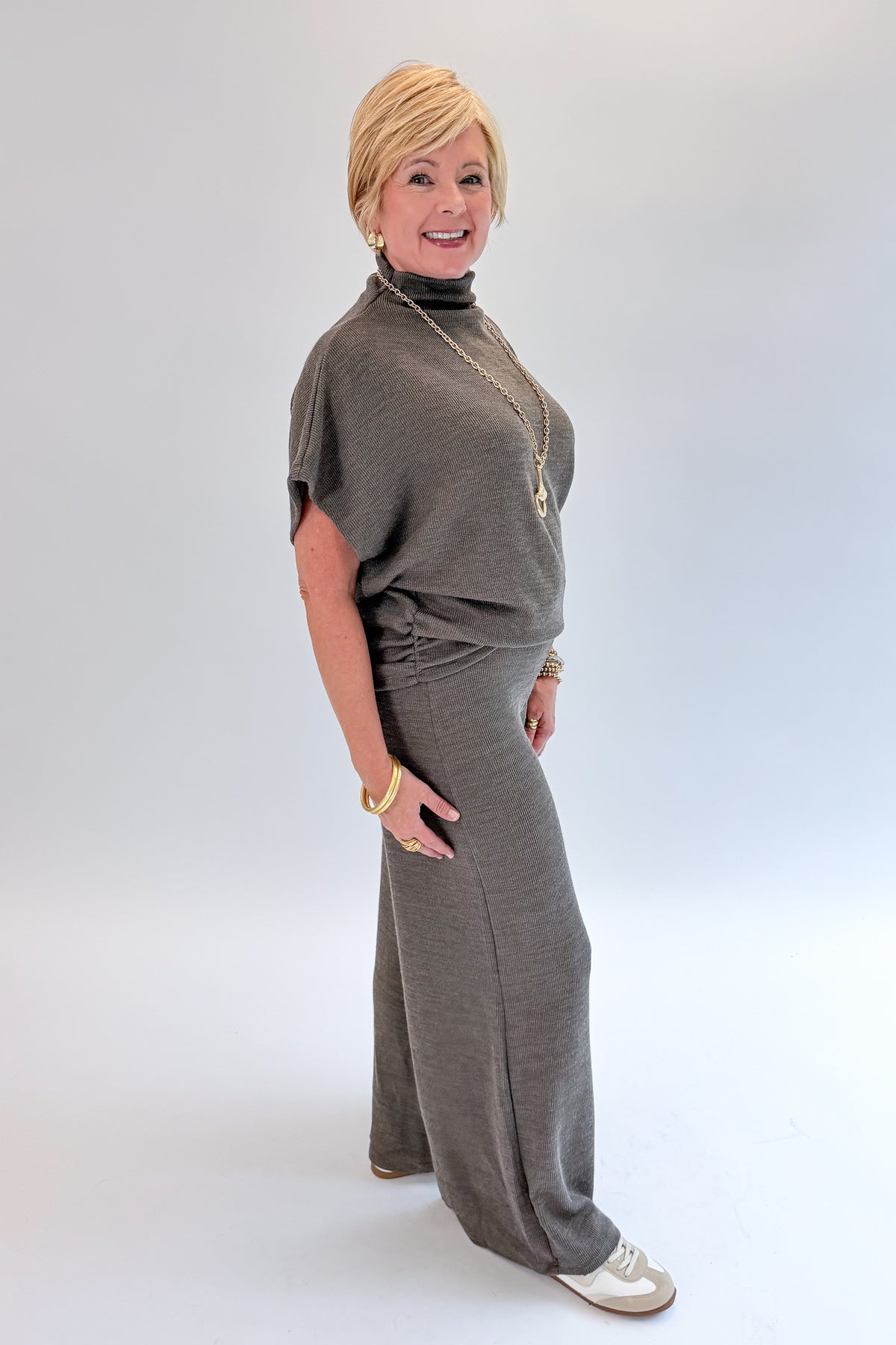 Side view of woman wearing Swagger Boutique’s Charcoal Ribbed Short Sleeve Turtleneck Top &amp; Lounge Pants against white studio background.