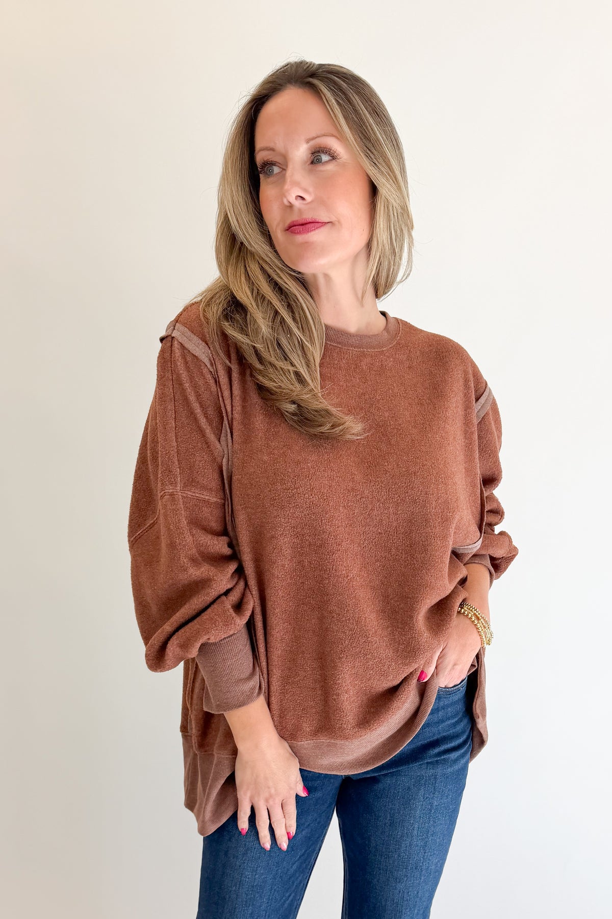 Front view of woman wearing Swagger Boutique’s Chestnut Seam Detail Sweatshirt with jeans against white studio background.