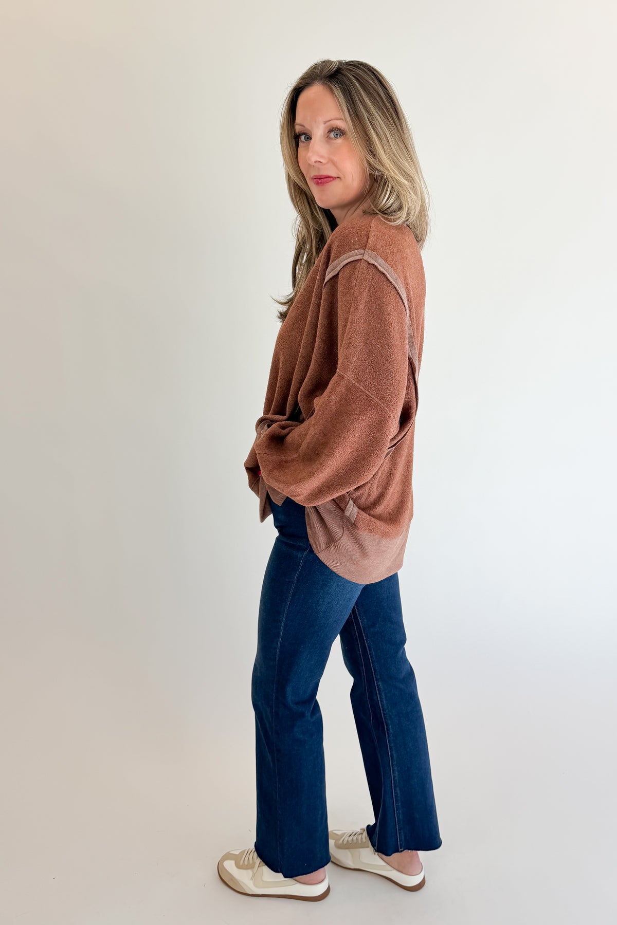 Side view of woman wearing Swagger Boutique’s Chestnut Seam Detail Sweatshirt with jeans against white studio background.