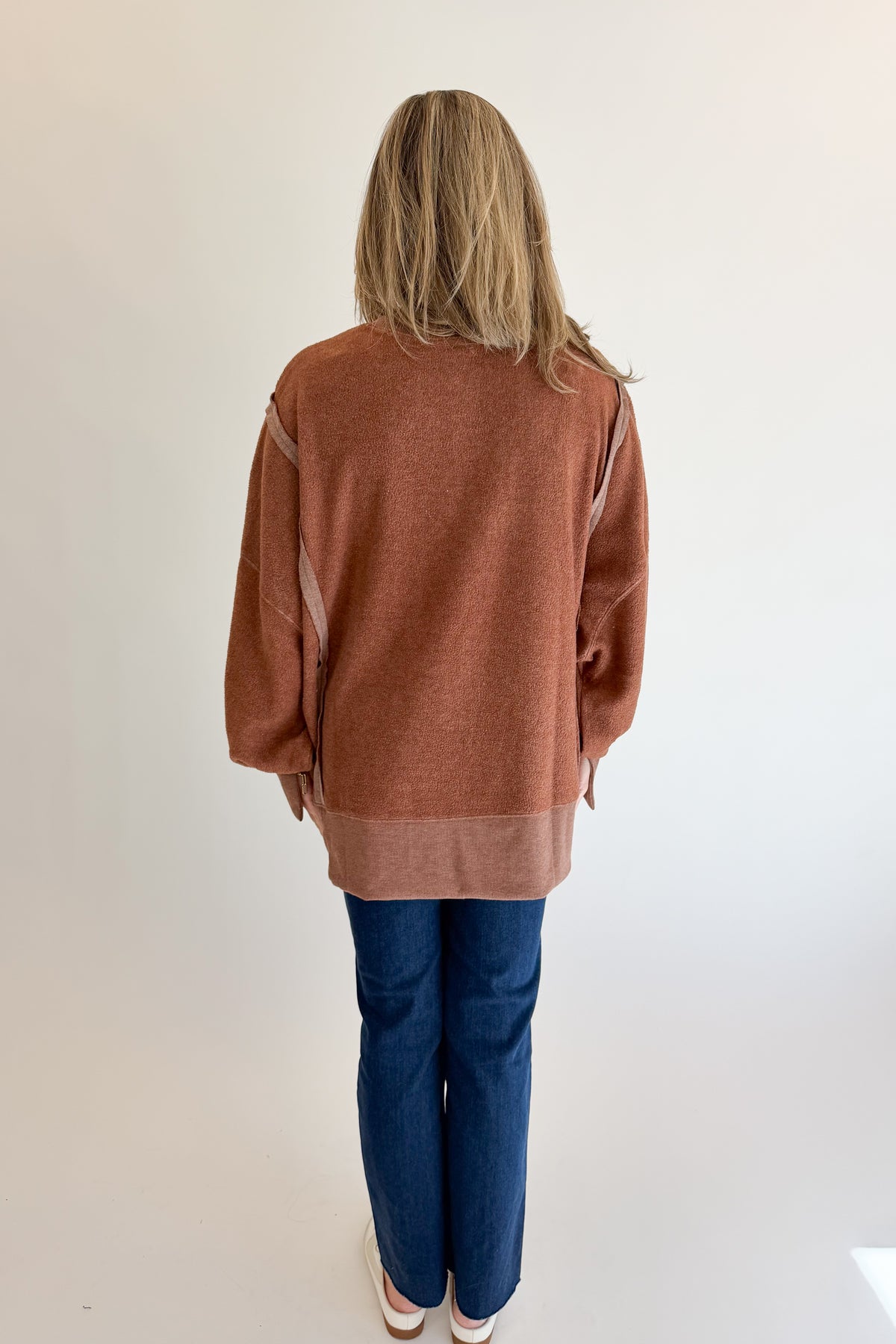 Back view of woman wearing Swagger Boutique’s Chestnut Seam Detail Sweatshirt with jeans against white studio background.