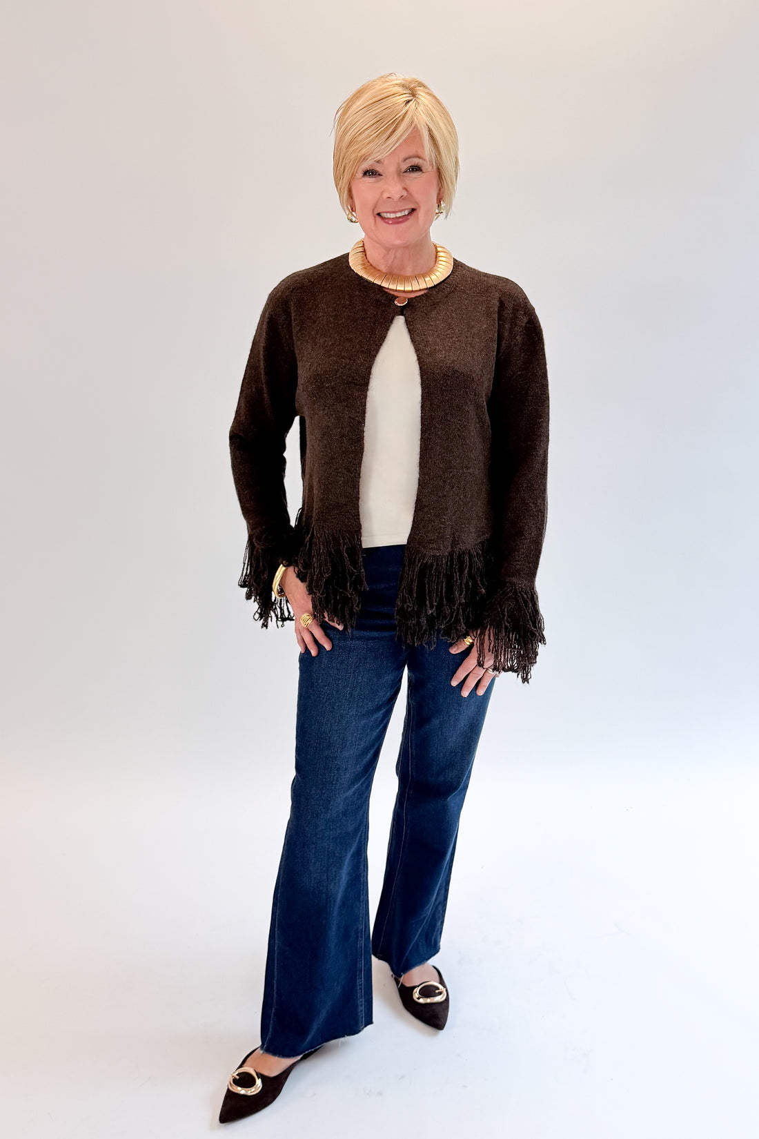 Front view of woman wearing Swagger Boutique’s Chocolate Brown Fringe Cardigan with jeans against white studio background.