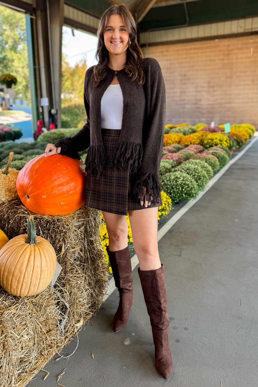 Front view of woman wearing Swagger Boutique’s Chocolate Brown Fringe Cardigan with jeans at a pumpkin patch.