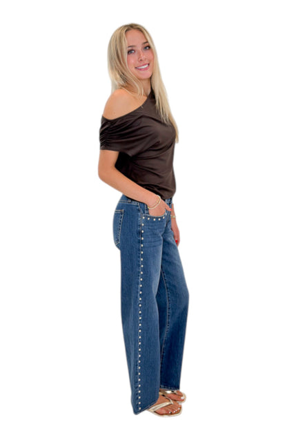 Side view of woman wearing Swagger Boutique’s Chocolate Brown Off The Shoulder Top with jeans against white studio background.