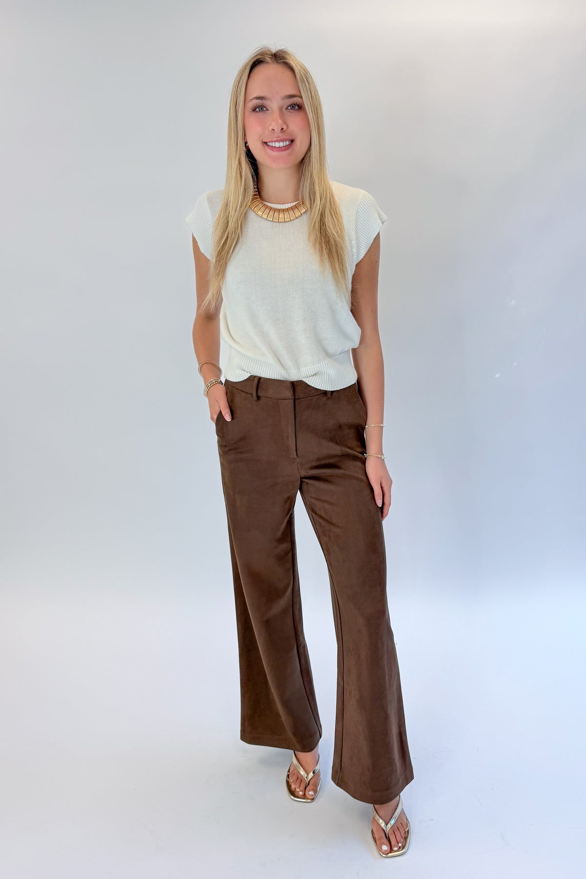 Front view of woman wearing Swagger Boutique’s Chocolate Brown Suede Pants with Living My Best Life White Cap Sleeve Sweater by PINCH against white studio background.