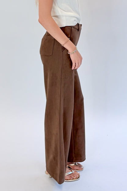 Side view of woman wearing Swagger Boutique’s Chocolate Brown Suede Pants with Living My Best Life White Cap Sleeve Sweater by PINCH against white studio background.